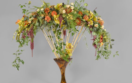 floral arrangement in a brown vase with small bamboo rods and yellow and orange flowers hanging at the top of the rods